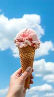 Hand holding strawberry ice cream with cone isolated on a blue sky and cloud background. ai generated photo