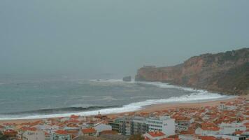 Nazare coast scene with oceanfront hotels and lighthouse on the rock, Portugal video