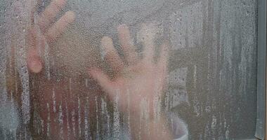 Kid wiping steamy window to look outside video