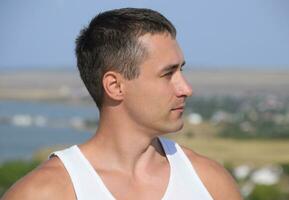 man in a white T-shirt in profile against the backdrop of a coastal village. photo