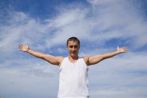 man in a white T-shirt laid his hands wide against the blue sky with clouds. photo