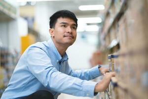 contento asiático hombre en azul camisa cheque productos en supermercado almacén inventario. importar y exportar negocio. foto