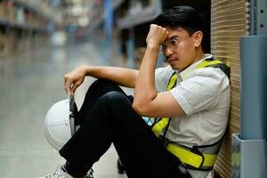 An Asian warehouse worker who is tired from work. Getting fired from a job. Unemployed. Failed. Desperate. photo