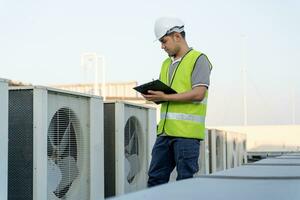 Asian maintenance engineer works on the roof of factory. contractor inspect compressor system and plans installation of air condition systems in construction. Checklist, inspector, control photo