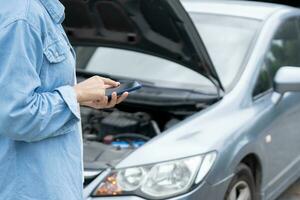 breakdown, broken car, repair. Woman uses mobile phone check insurance premiums through application due to car accident . Find garage to get car fixed during country tour, waiting for help, emergency. photo