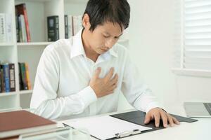 hand hold chest with heart attack symptoms, asian man working hard have chest pain caused by heart disease, leak, dilatation, enlarged coronary heart, press on the chest with a painful expression photo