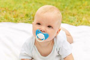 Cute little newborn girl lying on tummy on blanket in lawn on sunny summer day outdoor. Infant having fun outdoors. Infant baby child resting playing learning to crawl. Motherhood happy child concept. photo