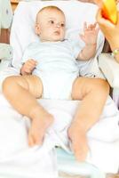 linda pequeño recién nacido niña con sonriente cara mirando a cámara en blanco antecedentes. infantil bebé descansando jugando acostado abajo en alimentación silla a hogar. maternidad contento niño concepto. foto