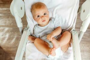 linda pequeño recién nacido niña con sonriente cara mirando a cámara en blanco antecedentes. infantil bebé descansando jugando acostado abajo en alimentación silla a hogar. maternidad contento niño concepto. foto