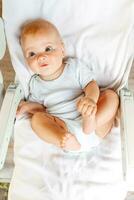 linda pequeño recién nacido niña con sonriente cara mirando a cámara en blanco antecedentes. infantil bebé descansando jugando acostado abajo en alimentación silla a hogar. maternidad contento niño concepto. foto