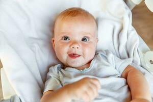 Cute little newborn girl with smiling face looking at camera on white background. Infant baby resting playing lying down on crib bed at home. Motherhood happy child concept. photo