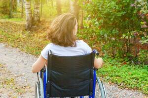 Young happy handicap woman in wheelchair on road in hospital park enjoying freedom. Paralyzed girl in invalid chair for disabled people outdoor in nature. Rehabilitation concept. photo