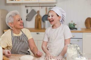 Happy family in kitchen. Grandmother and granddaughter child cook in kitchen together. Grandma teaching kid girl knead dough bake cookies. Household teamwork helping family generations concept. photo