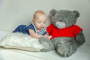 Infant baby boy lies on pillow with teddy bear toy on white bedroom background photo