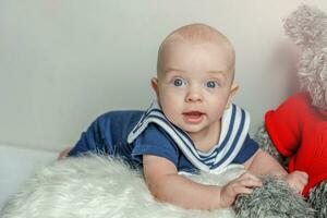 Infant baby boy lies on pillow with teddy bear toy on white bedroom background photo