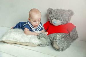 Infant baby boy lies on pillow with teddy bear toy on white bedroom background photo