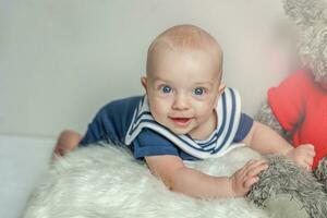 Infant baby boy lies on pillow with teddy bear toy on white bedroom background photo