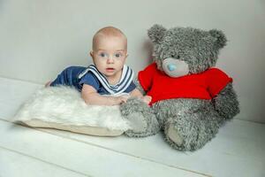 Infant baby boy lies on pillow with teddy bear toy on white bedroom background photo