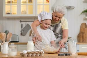 Happy family in kitchen. Grandmother and granddaughter child cook in kitchen together. Grandma teaching kid girl knead dough bake cookies. Household teamwork helping family generations concept. photo