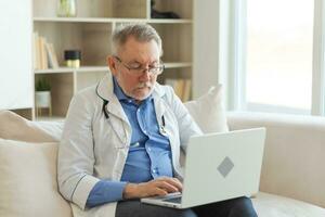 mayor hombre médico trabajando con ordenador portátil computadora. profesional mayor maduro cuidado de la salud experto buscando información o tener consulta en línea en hospital habitación. medicina cuidado de la salud médico chequeo. foto