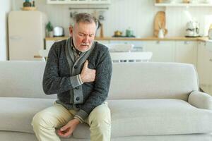 Pain on heart, heart attack. Unhappy middle aged senior man suffering from chest pain heart attack problems with health at home. Mature old senior grandfather touching chest experiencing infarction. photo