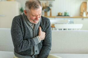 Pain on heart, heart attack. Unhappy middle aged senior man suffering from chest pain heart attack problems with health at home. Mature old senior grandfather touching chest experiencing infarction. photo