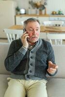 Happy middle aged senior man talking on smartphone with family friends. Older mature grandfather with cell phone talking with grown up children, resting at home. Older generation modern tech usage. photo