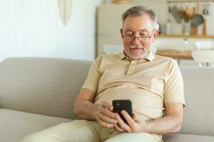 Happy middle aged senior man holding using smartphone touch screen typing scroll page. Stylish older mature beard grandfather with cell phone using internet social media apps at home. Shopping online. photo