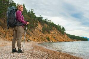 Hiking tourism adventure. Backpacker hiker woman looking at beautiful view. Hiker girl lady tourist with backpack walking near lake. Young happy woman enjoy hike trekking tourism active vacation. photo