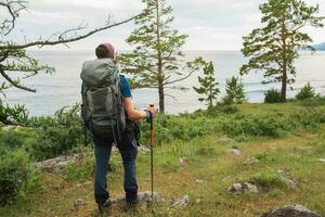 Hiking tourism adventure. Backpacker hiker man looking at beautiful view. Hiker tourist with backpack walking in green forest near lake. Back view man enjoy hike trekking tourism active vacation. photo