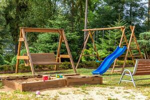 Empty modern wooden children playground set on green yard in public park in summer day. Funny toy land for kids. Urban exercise activities for child outdoors. Neighborhood childhood concept. photo