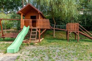 Empty modern wooden children playground set on green yard in public park in summer day. Funny toy land for kids. Urban exercise activities for child outdoors. Neighborhood childhood concept. photo
