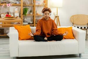 Yoga mindfulness meditation. Young healthy african girl practicing yoga at home. Woman sitting in lotus pose on yoga mat meditating smiling relaxing indoor. Girl doing breathing practice, yoga at home photo