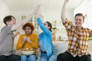 Group of friends watching sport match soccer football game on tv. Happy football fans celebrating victory at home. Friendship sports entertainment concept. Diverse buddies having fun together at home. photo