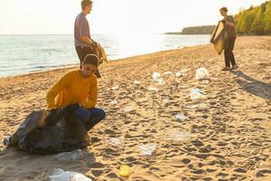 tierra día. voluntarios activistas recoge basura limpieza de playa costero zona. mujer y mans pone el plastico basura en basura bolso en Oceano costa. ambiental conservación costero zona limpieza. foto