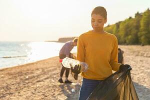 tierra día. voluntarios activistas recoge basura limpieza de playa costero zona. mujer pone el plastico botella basura en basura bolso en Oceano costa. ambiental conservación costero zona limpieza. foto