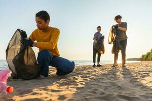 tierra día. voluntarios activistas recoge basura limpieza de playa costero zona. mujer y mans pone el plastico basura en basura bolso en Oceano costa. ambiental conservación costero zona limpieza. foto