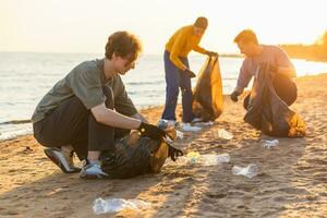 Earth day. Volunteers activists team collects garbage cleaning of beach coastal zone. Group of people puts plastic trash in garbage bags on ocean shore. Environmental conservation. photo