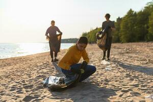 Earth day. Volunteers activists collects garbage cleaning of beach coastal zone. Woman and mans puts plastic trash in garbage bag on ocean shore. Environmental conservation coastal zone cleaning. photo