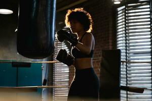 Women self defense girl power. African american woman fighter training punches on boxing ring. Healthy strong girl punching boxing bag. Training day in boxing gym. Strength fit body workout training. photo