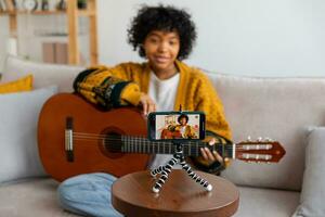 Blogger guitarist. African american girl blogger playing guitar talking to webcam recording vlog. Social media influencer woman streaming at home indoors. Music content creator broadcast tutorial. photo