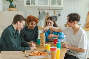 Home party. Friends spending time together playing in board game crash wooden tower at home. Happy diverse group having fun together indoor. Mixed race young buddies best friends enjoying weekend. photo