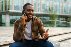 africano americano hombre hablando en teléfono inteligente en calle en ciudad exterior. hombre con célula teléfono chateando con amigos. sonriente persona haciendo respondiendo llamada por Teléfono móvil. chico teniendo conversacion por móvil. foto