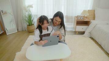 asiático pequeño joven niña aprendizaje en línea clase a hogar con madre foto