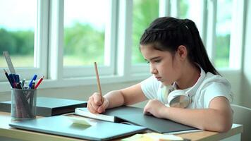 Cute young girl making notes in notebook at home desk. Distance learning concept. photo