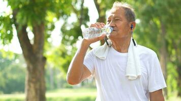 asiático mayor hombre o un abuelo, un contento retirado hombre con auriculares escuchando a radio música antes de hacer ejercicio en el parque. foto