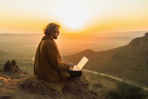 Digital nomad sitting on top of a hill working with his laptop over the city at sunset ,Generative AI. photo