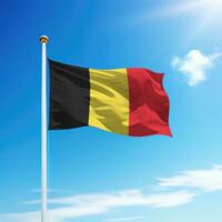ondulación bandera de Bélgica en asta de bandera con cielo antecedentes. foto