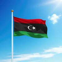 Waving flag of Libya on flagpole with sky background. photo