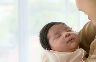 Cute newborn baby girl sleeping on mother arms near window at home photo